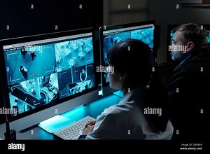 Two intercultural security guards in uniform sitting by workplace in front of computer monitors and observing cctv video on screens Stock Photo - Alamy