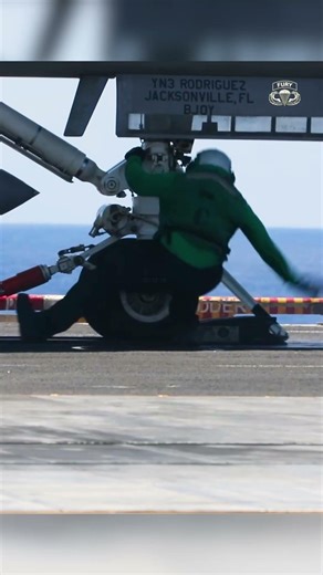 U.S. Sailors give hand signals for a flight over an aircraft carrier