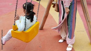 child having fun on a swing on the playground in public park.