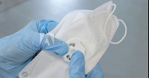 A worker in a protective suit connects a medical FFP3 mask. Hands insert the filter valve into the protective mask. Production of clothing for protection against the virus. Medicine clothing factory.