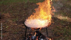 Flames erupt from a pan on a bonfire. Cooking in nature. Wilderness survival. Primitive cooking methods. Bonfire in the forest. Fire safety is important.