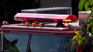 Red lights flash on a fire truck light bar up close in the USA at the scene of an emergency during the day.