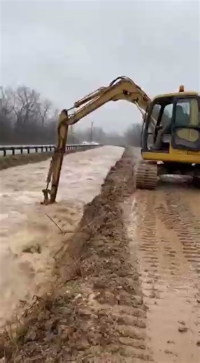 Video Shows Excavator Hanging on Cliff Edge as Floodwaters Eat Away Roadside Buncombe County, North Carolina – A dramatic roadside incident was caught on camera when an excavator nearly slid into floodwaters after erosion caused the edge of a washed-out road to collapse beneath it. The footage shows the excavator perched on a narrow embankment, its tracks gripping muddy soil as swollen floodwaters rush past just feet away. While clearing debris, the operator triggers a sudden collapse of earth, 