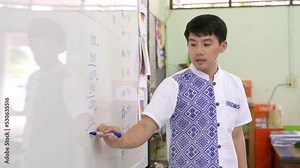 An Asian male teacher teaches math and writes the numbers on the board.