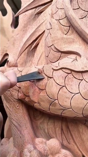 Hand using a sharp chisel to carve intricate overlapping scale patterns onto wood