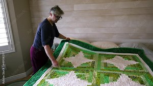 A senior woman shows a quilt that she made and explains the detail, design and process proudly