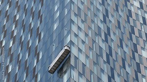 Skyscraper window cleaners working from suspended platform or scaffold on high rise building exterior glass wall.