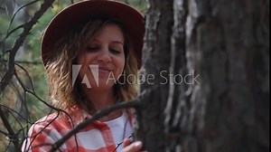 A beautiful adult curly woman touches the bark of a pine tree, hugs a large pine tree in the forest. Environment concept. Deforestation must be stopped because of the danger of climate change