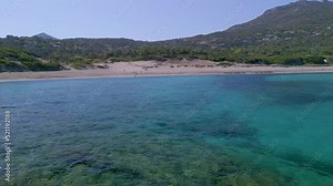 Aerial view pulling back across the translucent water of the Mediterranean sea away from the sandy beach of Bodri in the Balagne region of Corsica