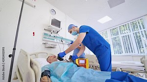 Male surgeon resuscitating an unconscious patient with a defibrillator in hospital. Nurse and male doctor in medical uniform help the patient in reanimation room.