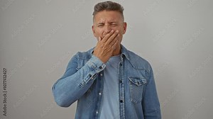 Middle-aged man yawning and stretching while wearing a denim jacket over a white background looking tired