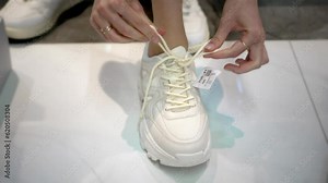 Girl with close-up of her legs and tries on shoes in fashion boutique. She chooses white sneakers, around lot of boxes and shelves with styles. Buying shoes and trying them on.