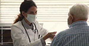 Female nurse practitioner doctor wear surgical face mask talk to senior male patient at meeting at hospital, provide professional qualified aid, medicare health insurance program for seniors concept