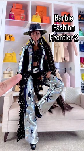 Barbie Fashion Frontier Doll No. 2 The Barbie Fashion Frontier series features out-of-this-world looks that blend Wild West and space-chic for a totally fresh feel. The second doll in the series shines in a night-sky inspired look, with a black crop tank, shimmering fringed cape, and matching silver starburst-patterned chaps. She elevates the celestial style with a rhinestone-buckle belt, leather arm cuffs, and a wide-brimmed hat that instantly rocket her to star status. #barbiecollection #matte
