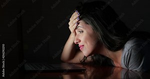 Woman reaction with frustration and annoyance in front of her laptop computer screen at night inside dark room