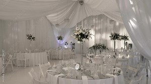 Wedding decoration of the banquet hall, ready to receive the newlyweds and guests. The camera moves along the round glass tables at the wedding banquet. Table setting with flower arrangement.