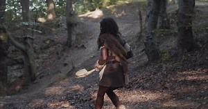 black caveman holding weapon wearing animal skin walk look around want to attack in prehistoric forest