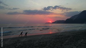 Aerial shot drone hovers at end of sunset as beach goers run along beach
