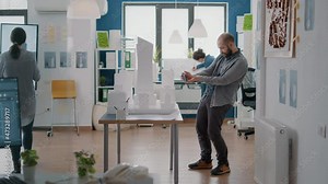 Architect using mobile phone to create blueprints plan with building model and maquette for construction development. Man engineer working with smartphone to design strategy project.