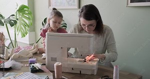 Mother and child daughter sewing together at home using sewing machine