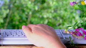 female hand tipping text on laptop keyboard in the garden against the background of green trees in summer, concept of the daily routine of a freelancer, programmer, downshifter