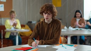 High school bullying upset stressed lonely Caucasian guy teen male boy schoolboy nerd student teenager writing task class desk university college children students mock bully throwing papers balls