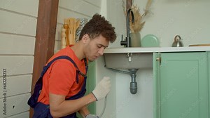 Professional attractive African American plumber in protective workwear fixing kitchen faucet, replacing and installing flexible water supply tubes while providing plumbing service indoors.
