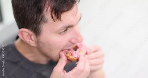 Man takes big bite of fresh donut enjoying sweet flavour. Male savours delicious cream-filled donut. Guy enjoys freshly baked donut