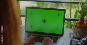 Woman typing on laptop with green screen on desk with photo camera and plant