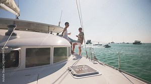 4K Caucasian couple enjoy luxury outdoor lifestyle with drinking champagne together while catamaran boat sailing in the sea. Confident man and woman relaxing on sail yacht on summer travel vacation