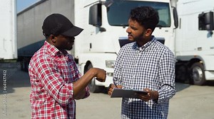 Indian manager and african trucker standing by truck with a clipboard, checking the delivery list