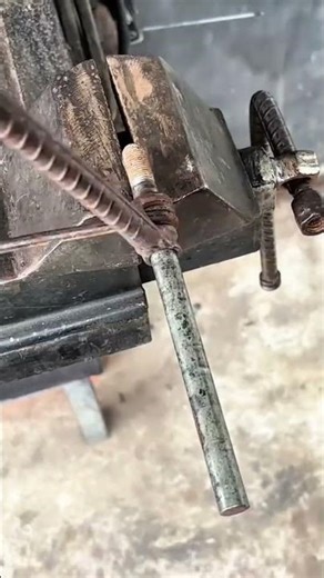 bending a long round metal rod using a heavy iron vice and a rebar handle in a workshop setting