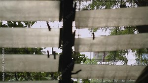 Steady, interior, medium wide shot of a window with glass and wired fence. Shack homes and some trees can be seen through the window.