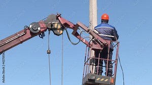 Electricians Wiring Cable repair services, worker in crane truck bucket fixes high voltage power transmission line, setting up the power line wire on electric power pole.