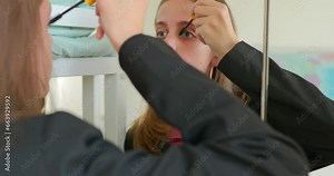 Teenage girl doing makeup while standing at the mirror