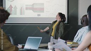 Young businesswoman with Down syndrome pointing at financial graphs on projection screen and giving presentation to colleagues during office meeting