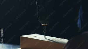 Slowmotion. Screwdrivers twists bolt in a piece of wood. Man using a steel drill and usual screwdriver on wooden plate, on black background, slow motion. Tightening a screw with a screwdriver.