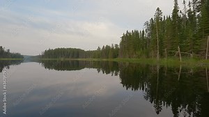GoPro footage from the front of a canoe of a calm late-day scene of a lake that is reflecting the surrounding forest.