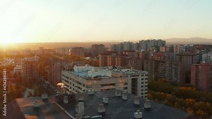 Fly over roof of apartment building on large housing estate. View against setting sun.