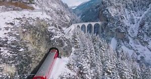 Landwasser Viaduct world heritage sight with luxury Glacier and Bernina express in Swiss Alps snow winter scenery. Aerial Drone shot red train passing through famous mountain in Filisur, Switzerland.