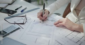 A young woman architect makes notes on invoice at her desk at her work office