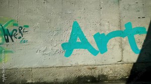 Sunlight progressively illuminates a vibrant blue graffiti on a white urban wall, creating a striking contrast between light and shadow in a modern city environment