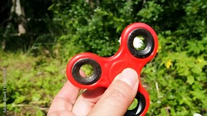Fidget red color in the hands is spinning on a nature. Toy anti-stress relaxation. Soothing and distracting object for tranquility.