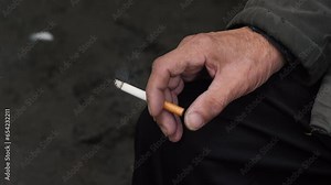 an old man of 70 years old smokes a cigarette while sitting on a bench, close-up of the hand of a pensioner holding a cigarette. life of real pensioners. elderly father smokes