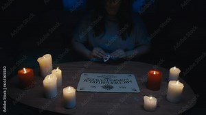 Video capturing a woman's figure having an ouija board session, seance, surrounded by candles in the dark. Planchette starts moving across the board. Stock Video