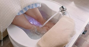 Feet being washed during a pedicure session at a spa. Water flows gently over feet, highlighting cleanliness and relaxation. Emphasizes professional care and serene environment.