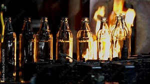 Glass bottles moving along a conveyor line fall under an open flame for glass hardening. Manufacture of glass bottles and glassware. Annealing glass bottles.