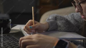 Close-up, teenage girl doing homework on the distance learning front of a laptop. Girl with a pencil writing in a notebook.