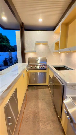 BBQ Islands & Designs on Instagram: "Fire. Flavor. Family. 🔥📺🍔 This outdoor kitchen brings everything together, a 55” TV for game nights, a Blaze grill for backyard feasts, and a cozy island for gathering under the patio lights. Designed for connection, built for luxury. ✔️ Media wall w/ 55” TV, dual side burners, fridge & ice chest ✔️ Stainless steel storage doors + shelving ✔️ L-shaped bbq island w/ Blaze Grill & drawers ✔️ Seats 4 under a full patio cover ✨ Drop “PRICE” in the comments for