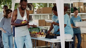 Friendly charity workers at food drive distributing necessities and free food to underprivileged. Voluntary individuals helping to fight hunger by providing hot meals to needy and homeless people.